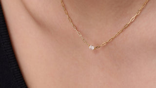 Gold necklace with a small pendant on a person wearing a black top.