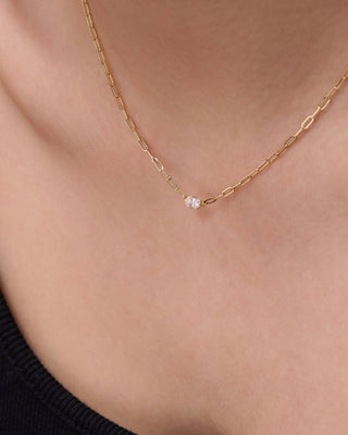 Gold necklace with a small pendant on a person wearing a black top.