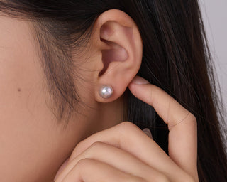 Close-up of a person wearing a pearl earring with a neutral background