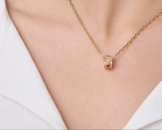 Gold necklace and earrings on a person wearing a white top against a neutral background