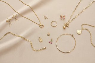 Gold jewelry including necklaces, bracelets, and earrings on a beige fabric background