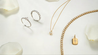 Gold jewelry including rings and a necklace on a white surface with white flowers.