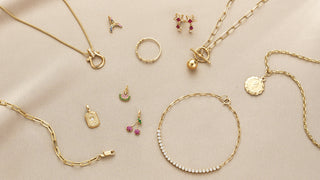 Collection of gold jewelry including necklaces, bracelets, and earrings on a beige background