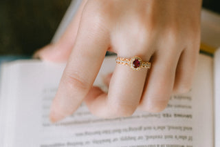 Close-up of a hand wearing a gold ring with a red gemstone on an open book.