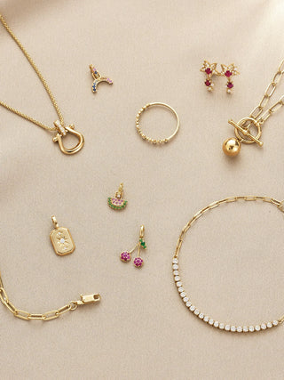 Collection of gold jewelry including necklaces, rings, and earrings on a beige background