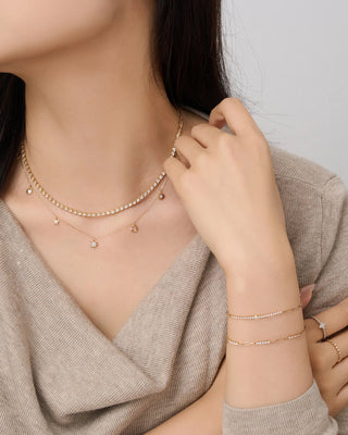 Woman wearing gold necklaces, bracelets, and rings on a plain background