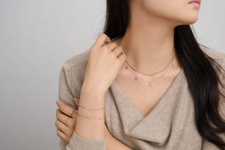 Woman wearing gold necklaces, bracelets, and rings on a plain background