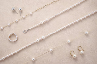 Pearl jewelry set including necklace, earrings, and ring on a beige background
