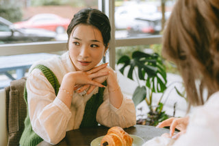 Woman sitting at a table with a pastry, engaged in conversation with another person.